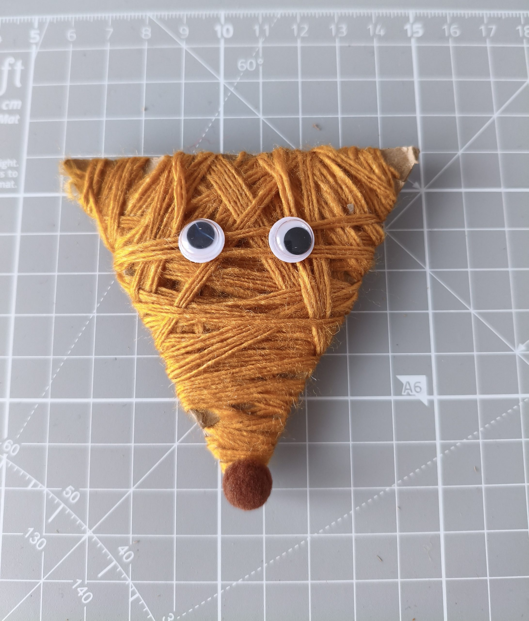 Głowa lisa wycięta z kartonu opleciona włóczką i umieszczonymi na nią oczami i noskiem.