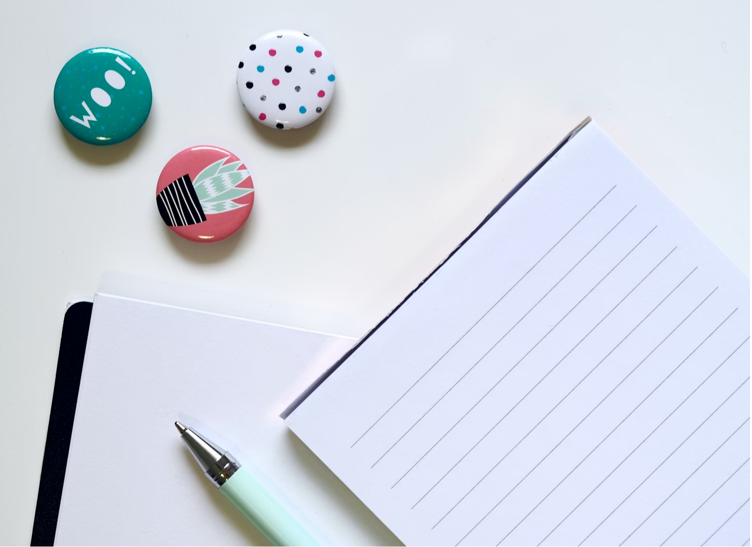 Zdjęcie przedstawiające przypinki, notes i długopisy.