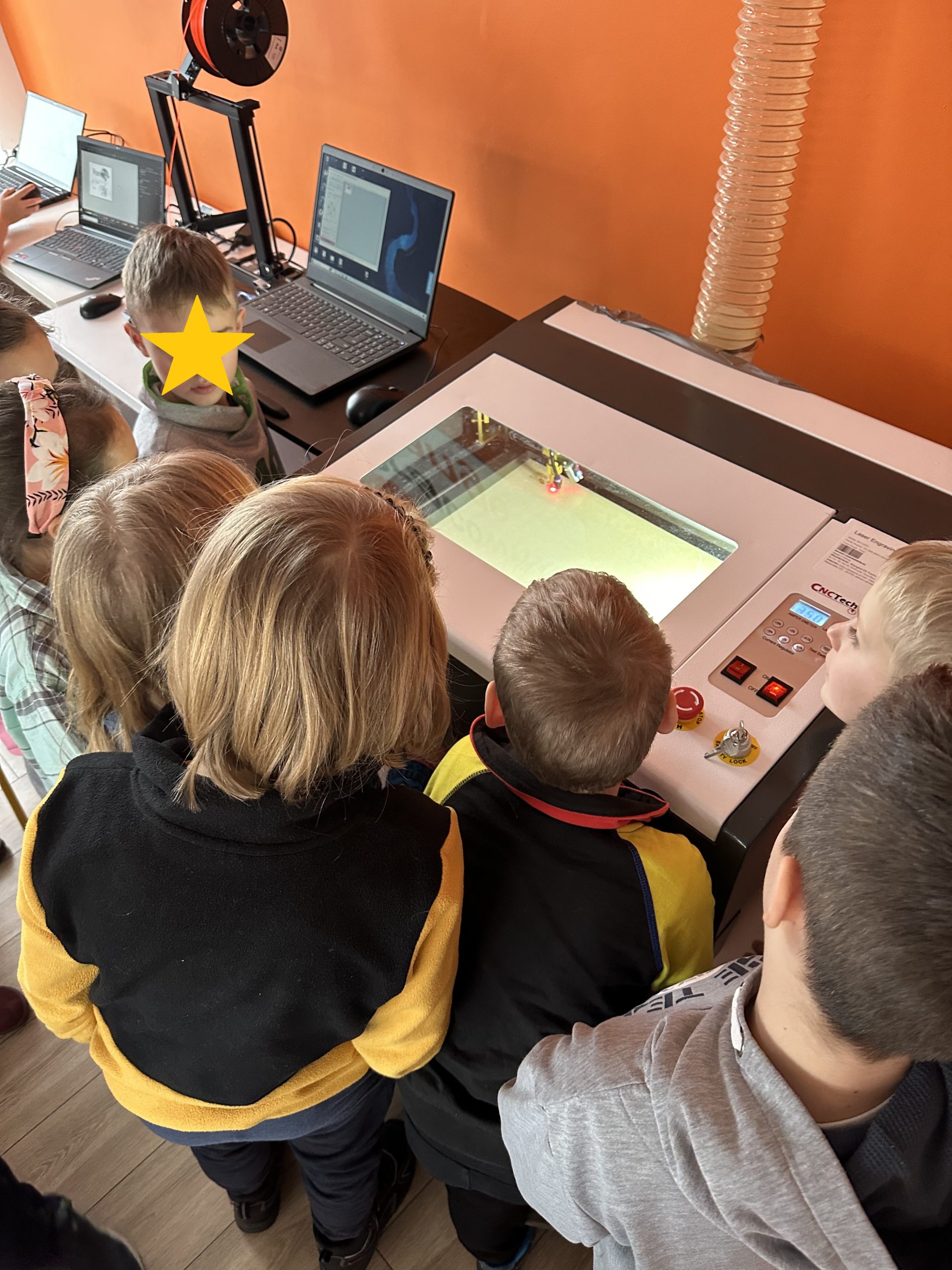 Zdjęcie. Grupa dzieci obserwuje działanie drukarki 3D.