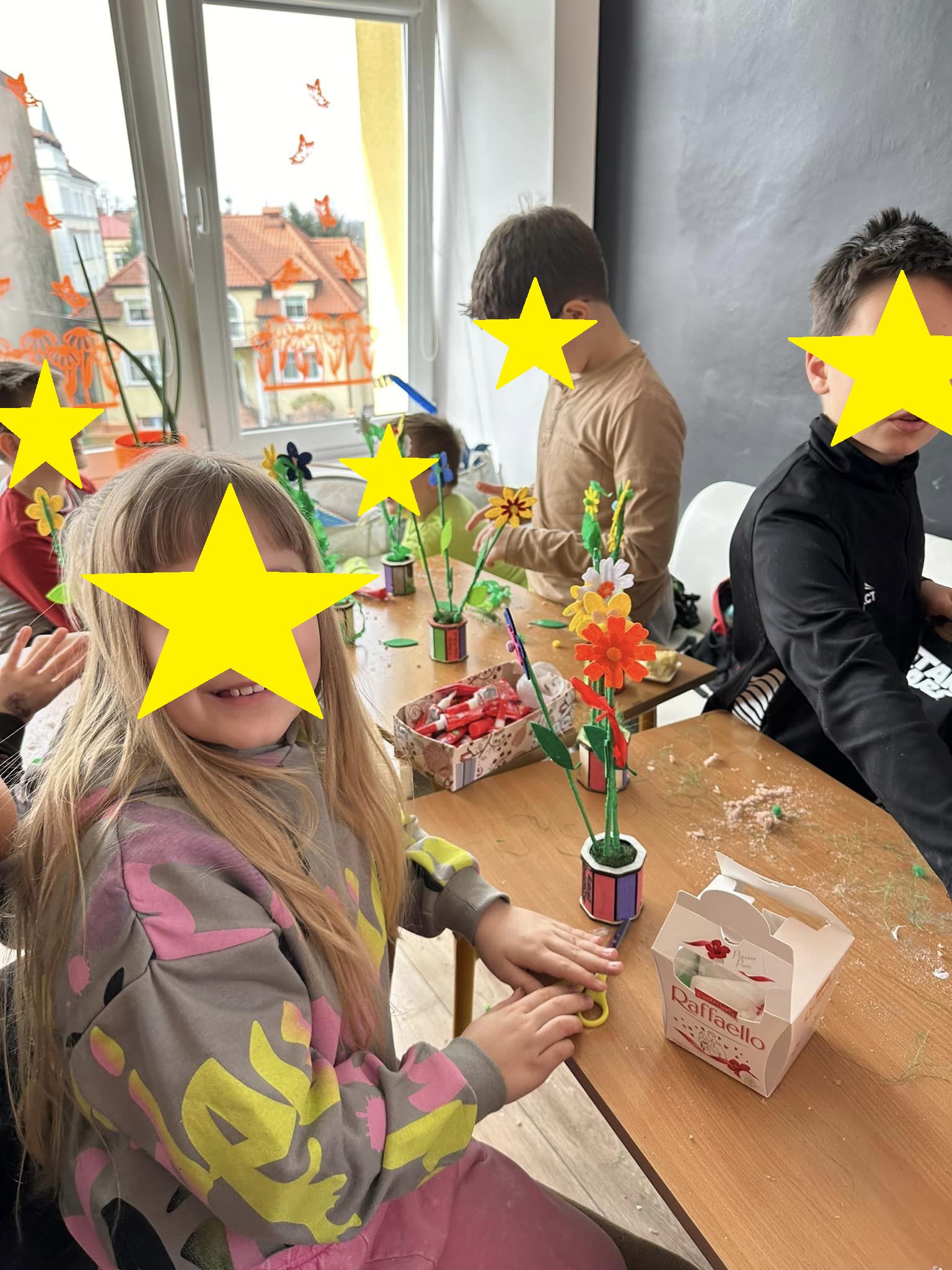 Grupa dzieci siedzi przy stole tworząc kwiatki.