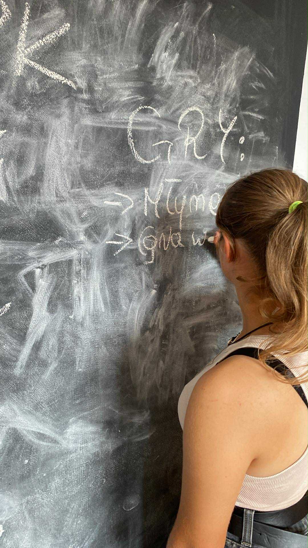 na zdjęciu dziewczyna pisząca kredą po tablicy