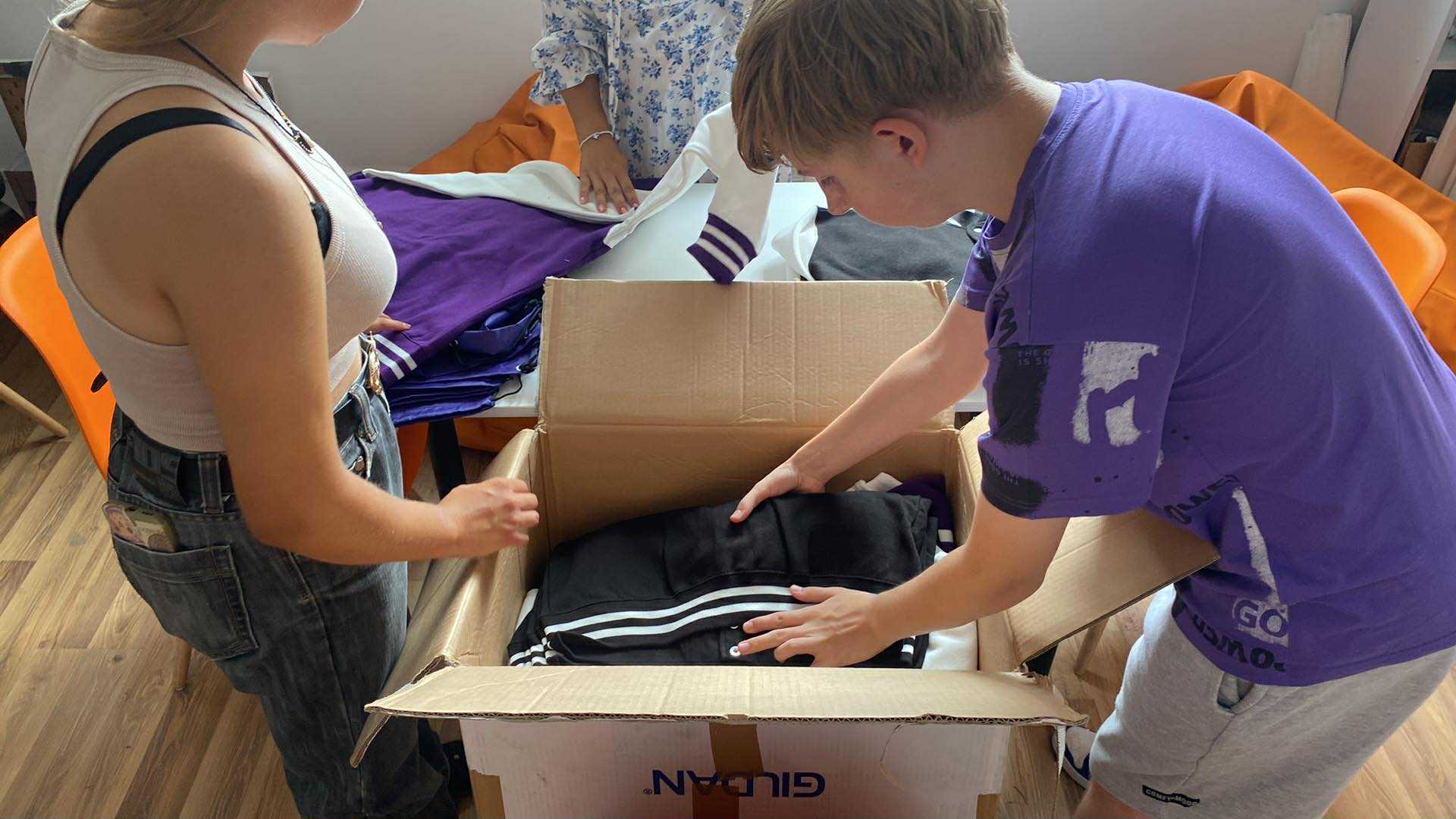na zdjęciu dwójka osób składająca bluzy do kartonu