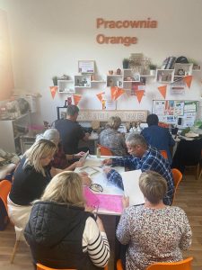 Uczestnicy warsztatów siedzą przy stołach w Pracowni Orange.