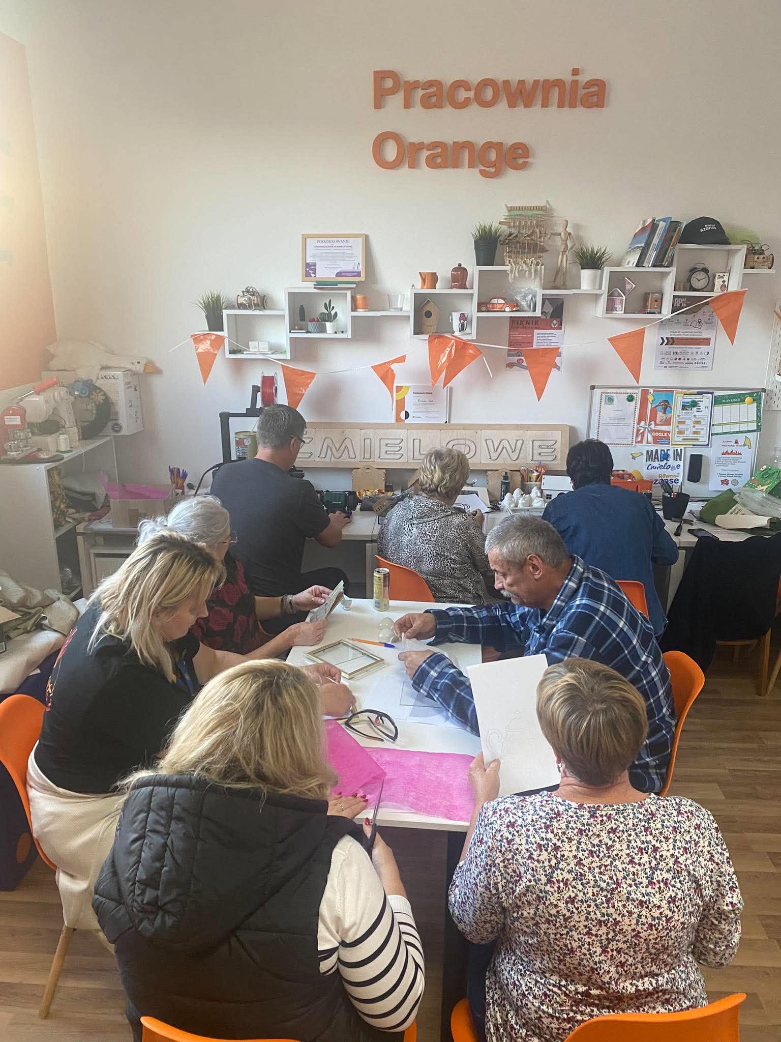 Uczestnicy warsztatów siedzą przy stołach w Pracowni Orange.