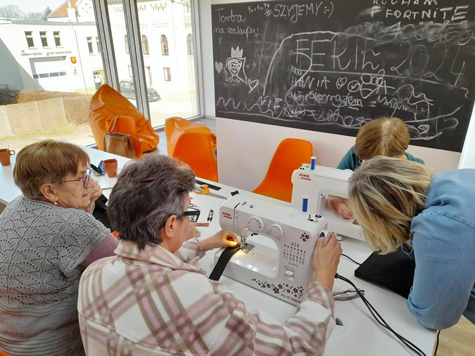 Cztery kobiety przy stole, dwie szyją na maszynach.