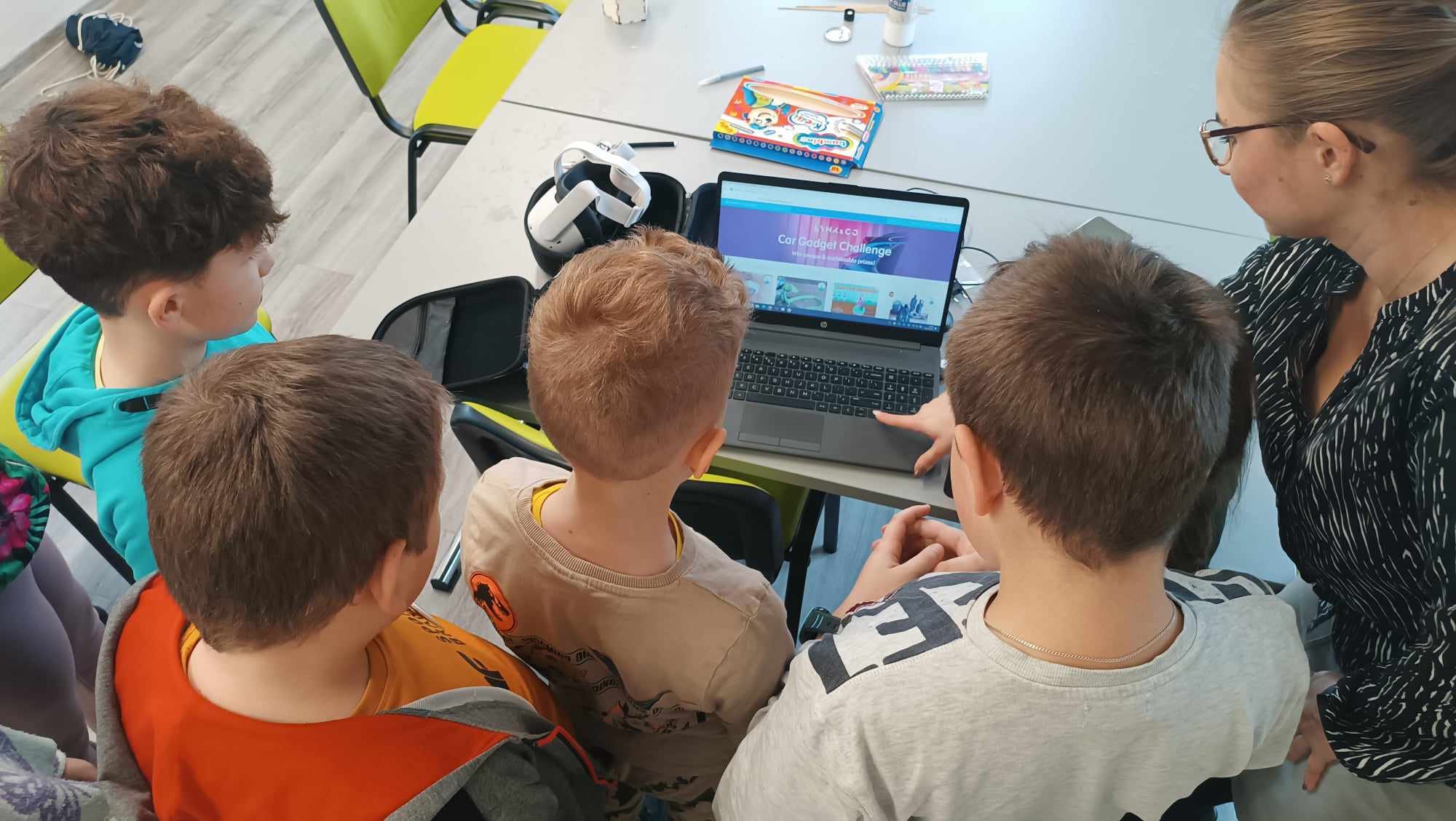 Grupa chłopców z prowadzącą zajęcia przed laptopem.