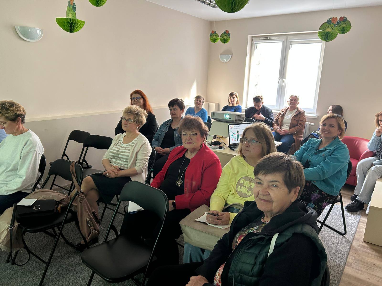 Grupa osób siedzących na krzesełkach - publiczność przybyła na spotkanie.