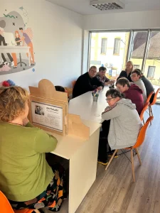 warsztaty w pracowni, grupa osób siedzi przy stoliku i ogląda teatr kamishibai