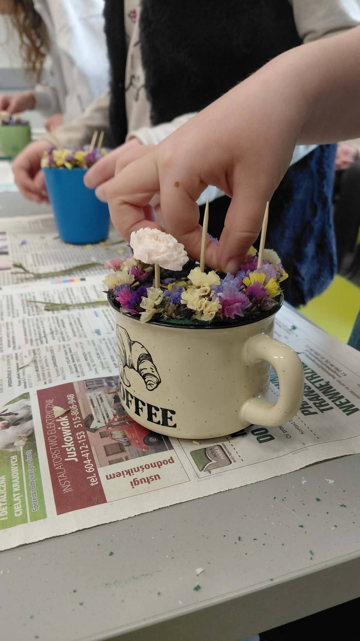 kubek z powstającą kompozycją kwiatków z mydła oraz zasuszonych kwiatów