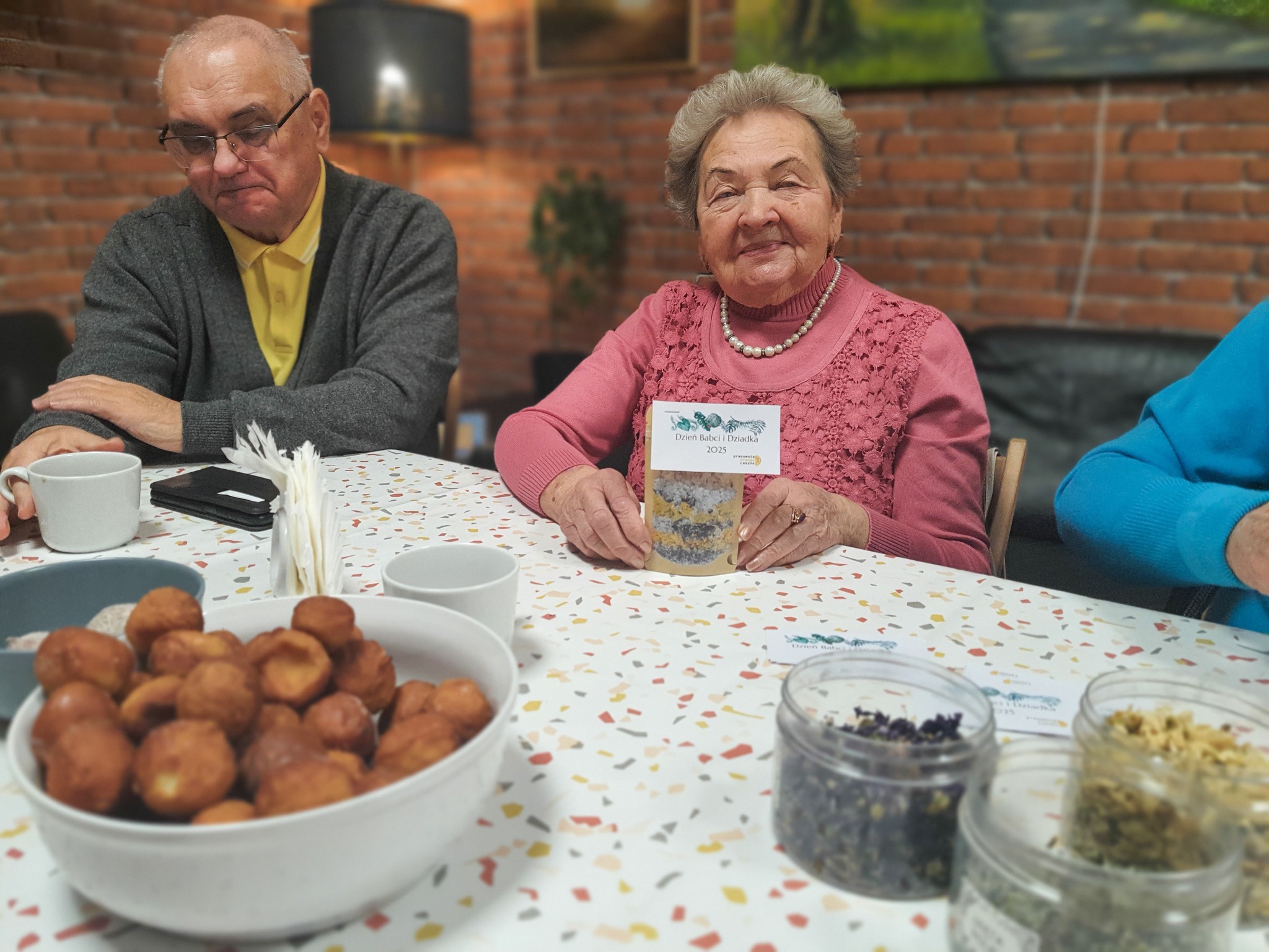 Seniorka siedząca przy seniorze prezentuje swoje sole kąpielowe