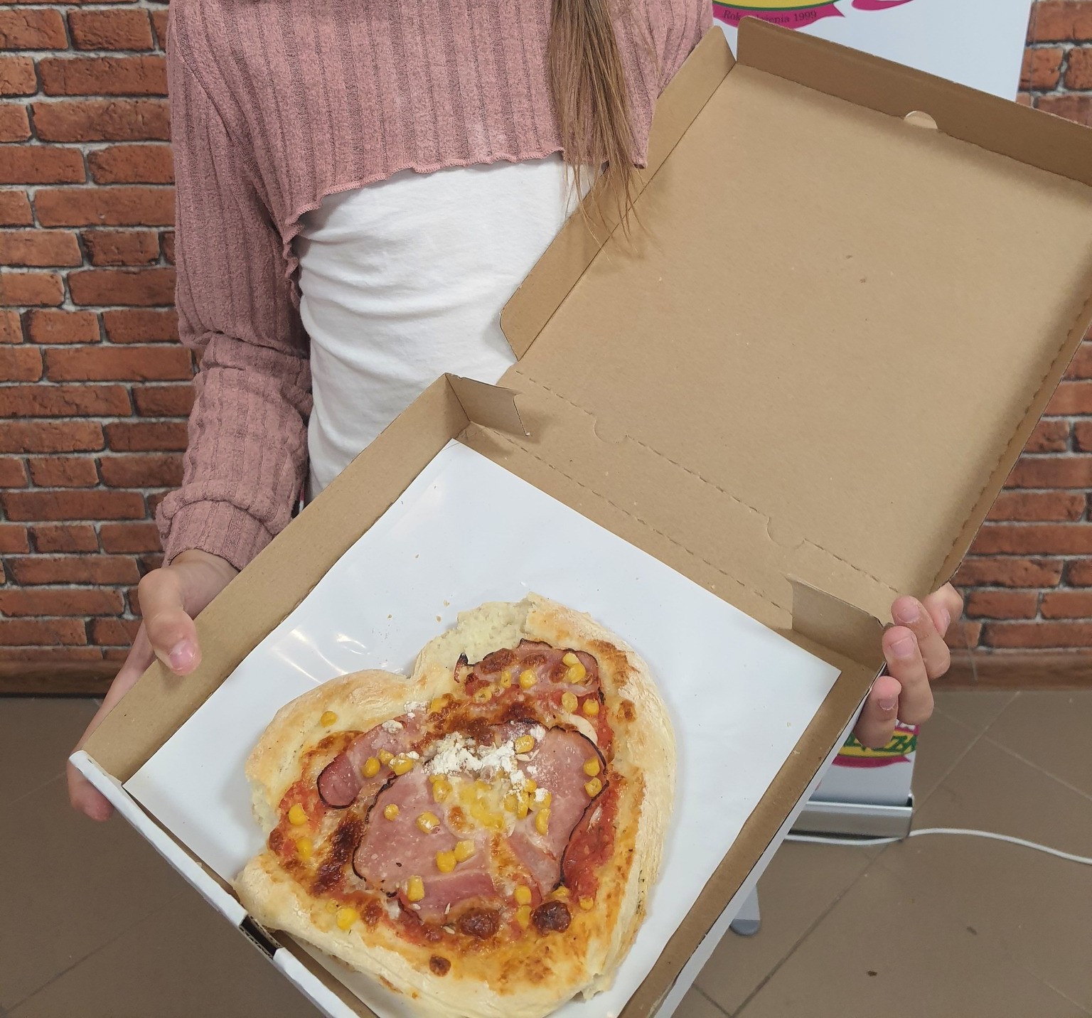 dziewczynka trzymająca w ręku pudełko z pizzą. pizza ma kształt serca.