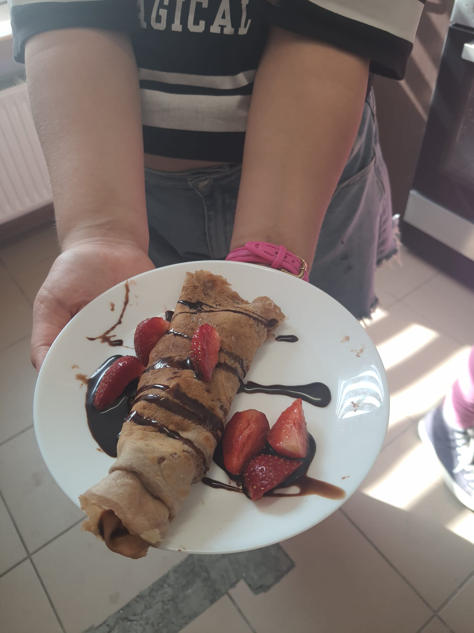 zbliżenie na ręce trzymające talerz z naleśnikiem polanym sosem czekoladowym z truskawkami