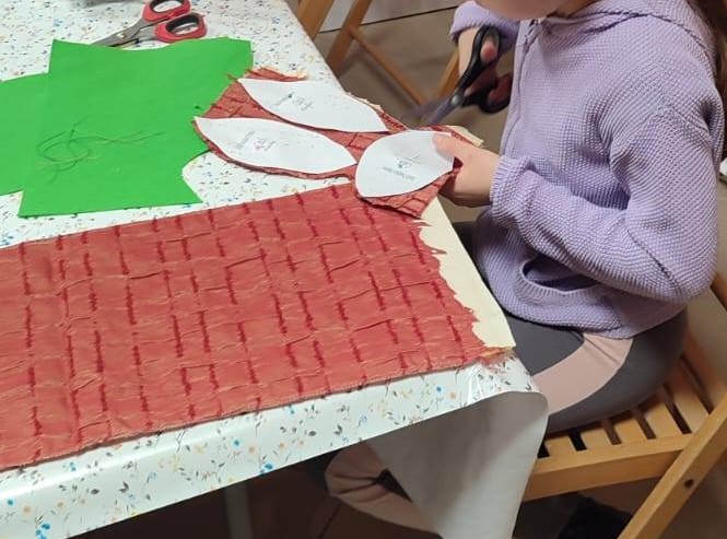 widać stół i dziecko ubrane na fioletowo wycinające z czerwonego materiału elipsy