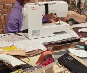 zbliżenie na maszynę do szycia i instruktorkę tłumaczącą korzystanie z niej dziecku