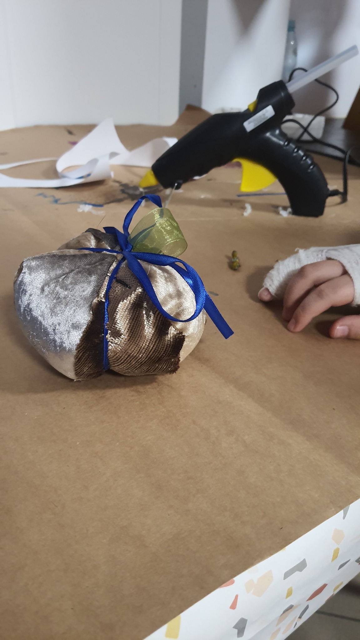 na brązowym blacie mateirałowa dynia w kolorze opalizującego brązu oraz dłoń dziecka w gipsie. w tel pistolet na klej.