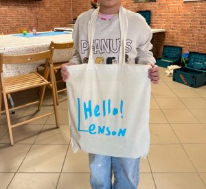 Dziecko prezentuje białą torbę z własnoręcznie wykonanym napisem „Hello! Lenson"