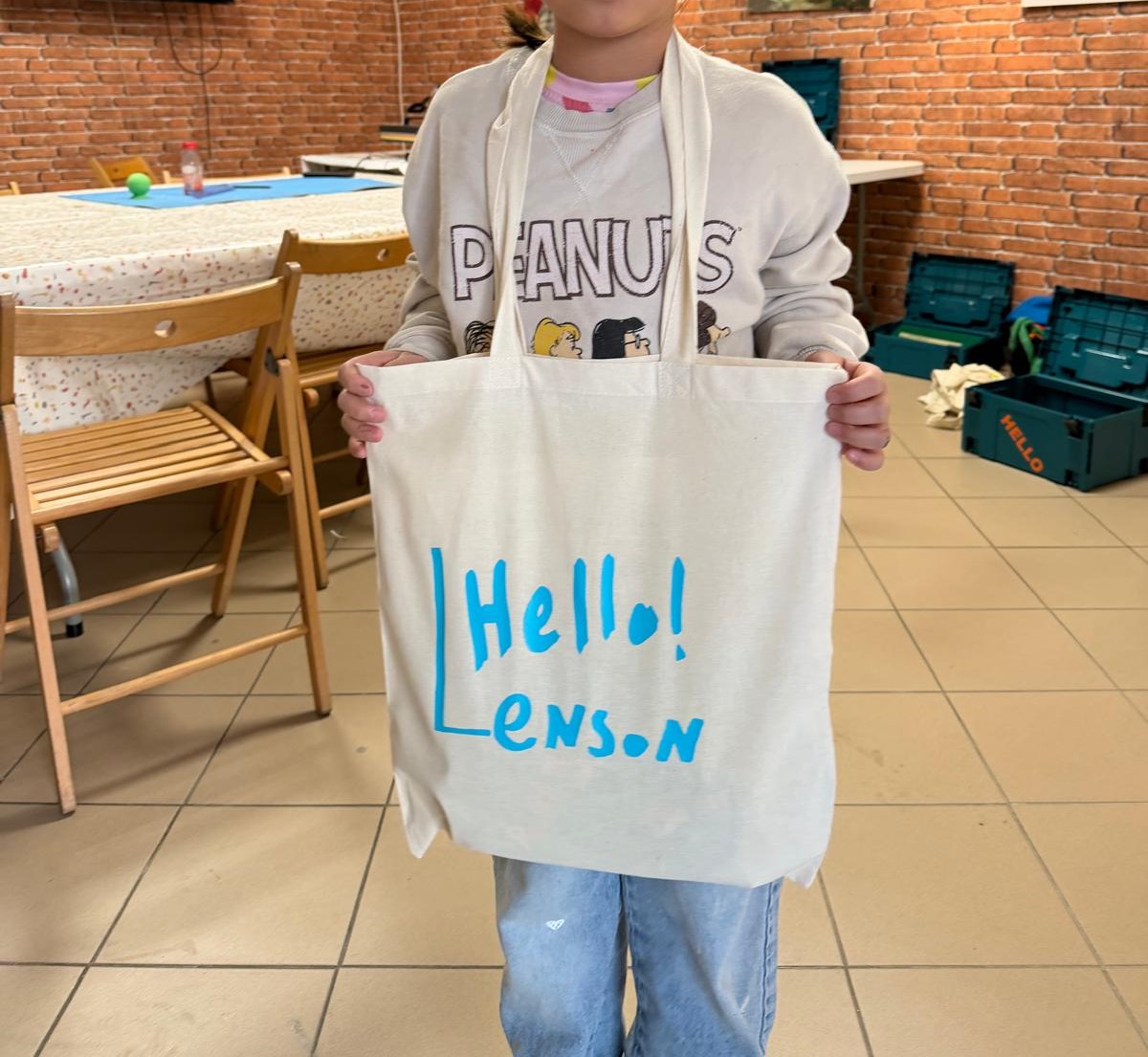 Dziecko prezentuje białą torbę z własnoręcznie wykonanym napisem „Hello! Lenson"