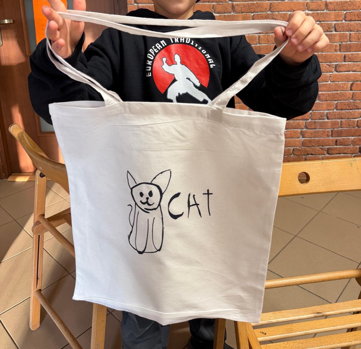 Dziecko trzyma białą torbę ozdobioną rysunkiem kota i napisem „CAT”
