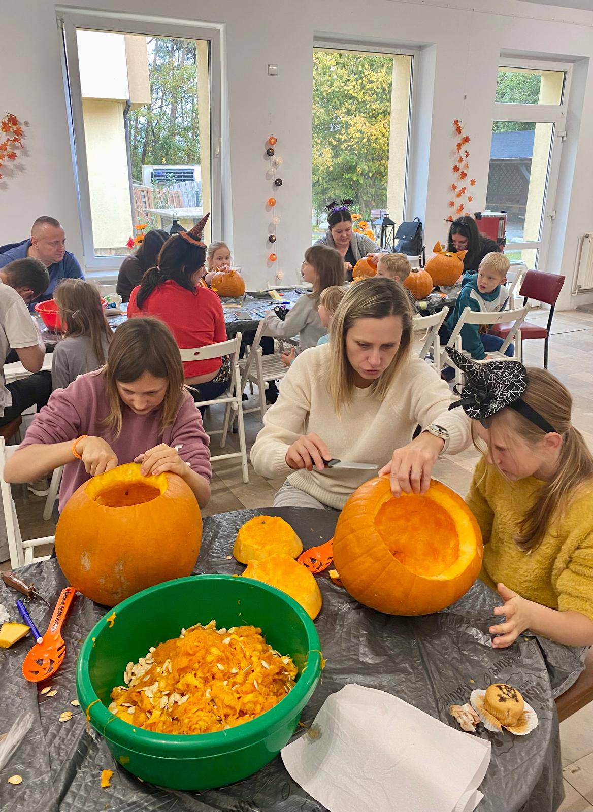 Uczestnicy warsztatów tworzą lampiony, trzy osoby przy stole wycinają fragmenty dyni.