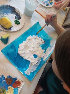 dziecko domalowuje niebieskie tlo , naklejony jest niedźwiedź biały , który pokryty jest białą bibułą