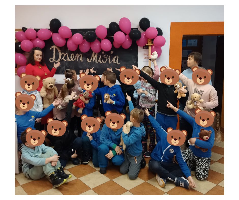 zdjęcie zbiorowe dzieci z maskotkami i maskami misiów z dorosłymi nauczycielkami na tle napisu Dzień Misia