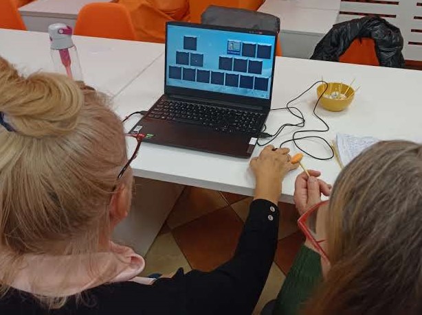 Na zdjęciu widoczne są uczestniczki zajęć siedzące przed laptopem na którym widoczna jest gra w memory.