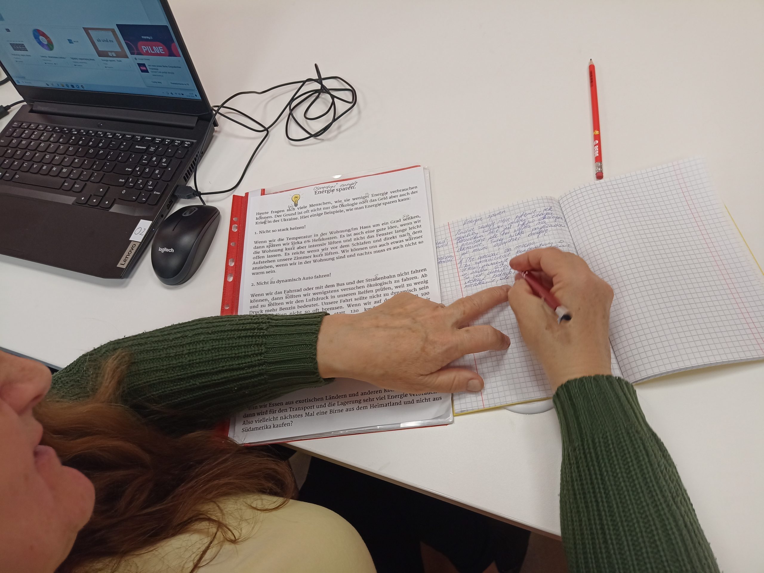 Na zdjęciu widoczne dłonie osoby dorosłej, która zapisuje słowa z niemieckiego tekstu w zeszycie.
