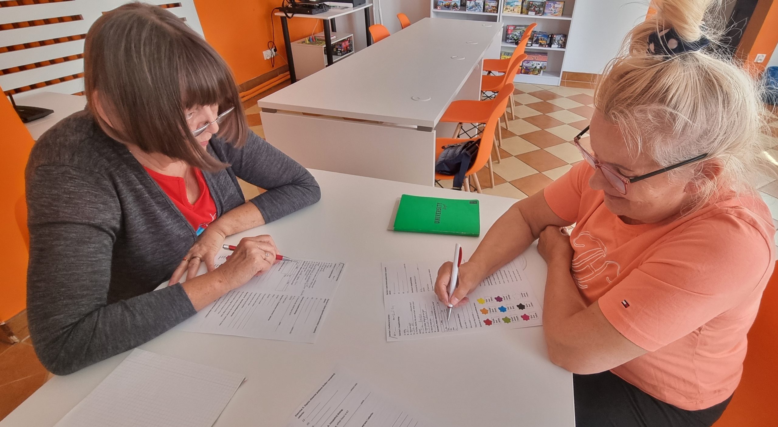 zdjęcie seniorek podczas rozwiązywania testu przy biurku w pracowni orange