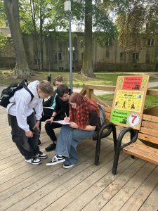 zdjęcie młodzieży na ławce w parku podczas wpisywania rozwiązania zadania obok tablicy korkowej