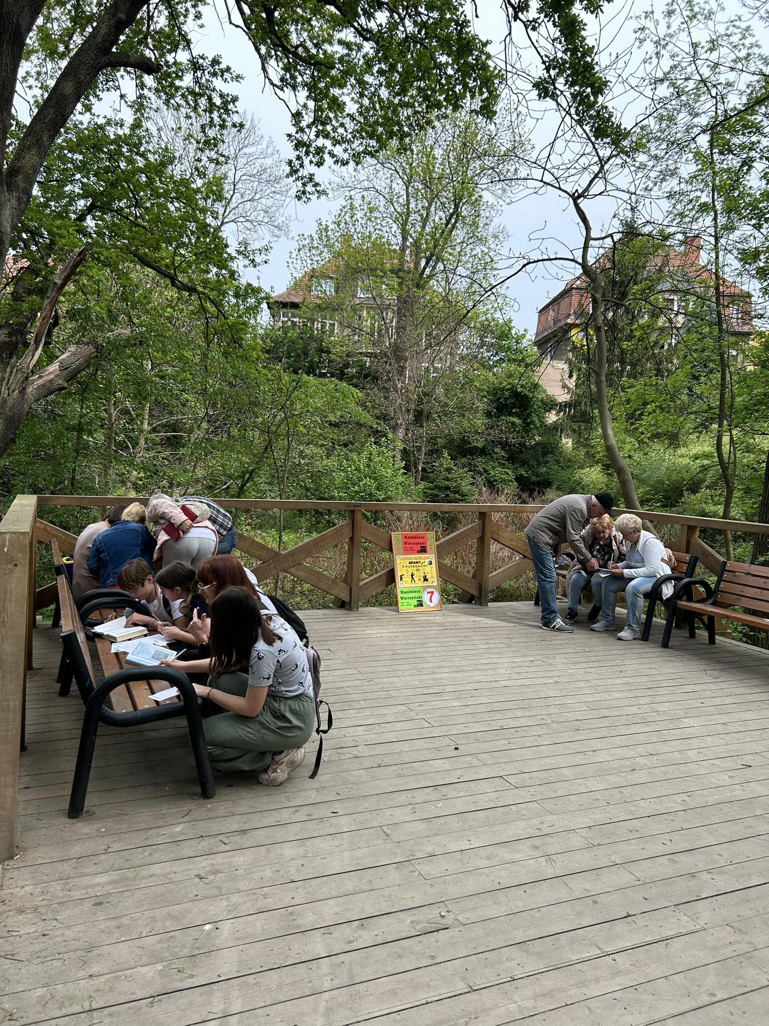 zdjęcie grup młodzieży i dorosłych podczas rozwiązywania zadań na ławkach w parku