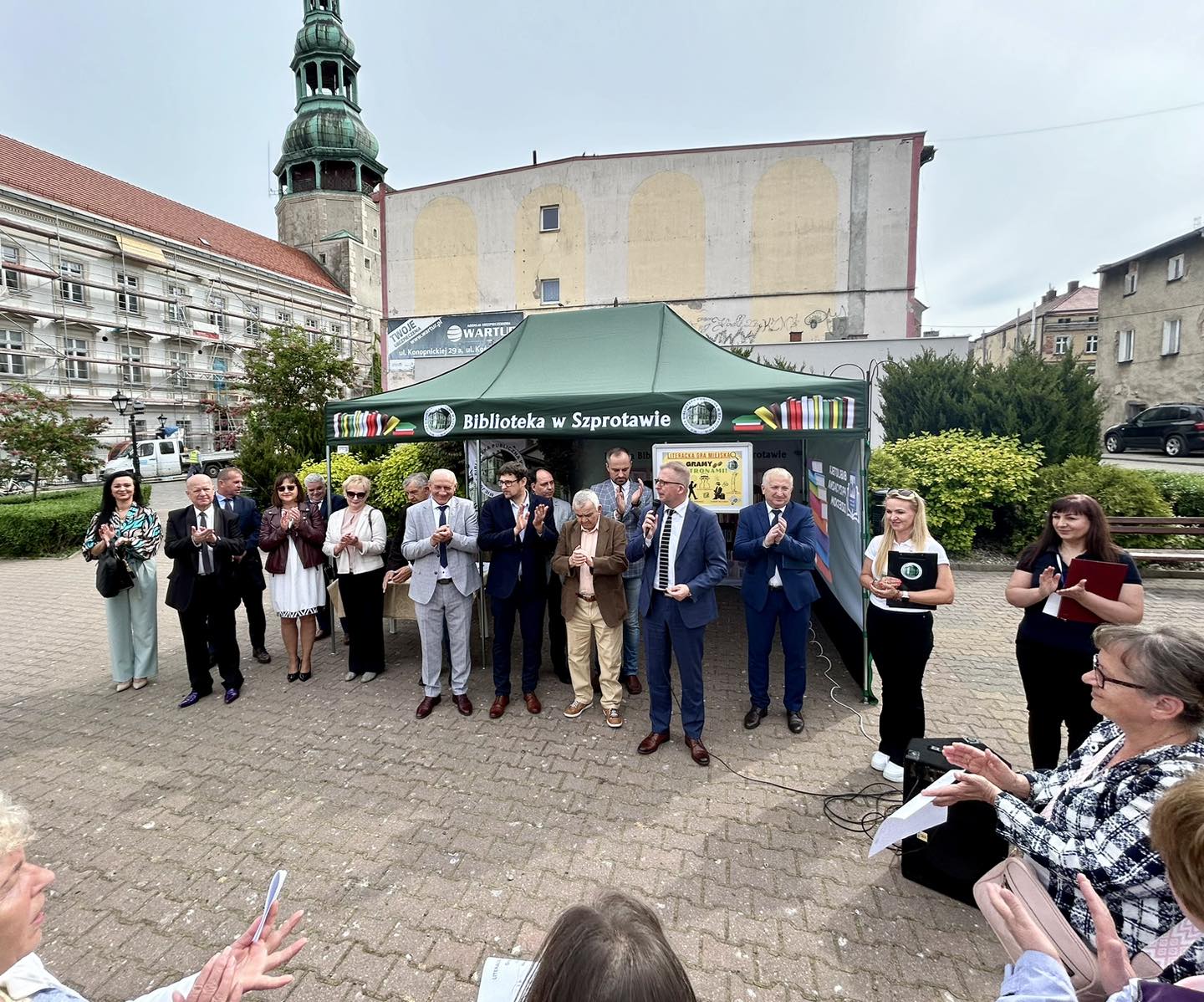 zdjęcie burmistrza Szprotawy, radnych miejskich oraz dyrektor biblioteki z bibliotekarką podczas otwarcia gry miejskiej na placu przed ratuszem