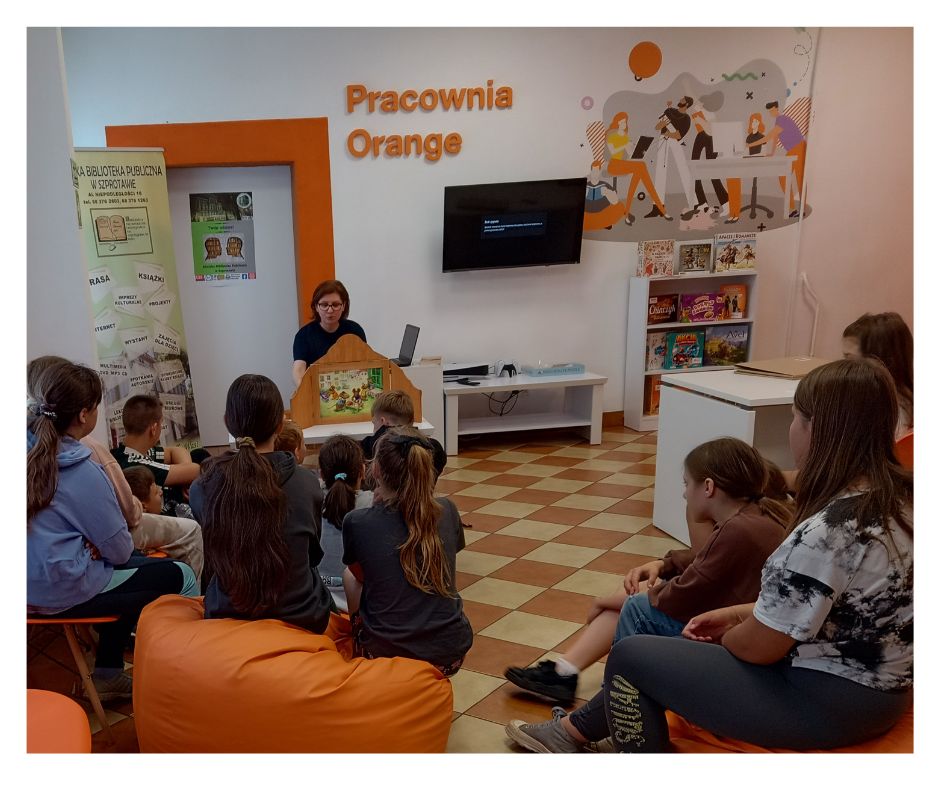 grupa młodzieży ogląda jak prowadząca prezentuje teatrzyk kamishibai w pomieszczeniu pracowni orange