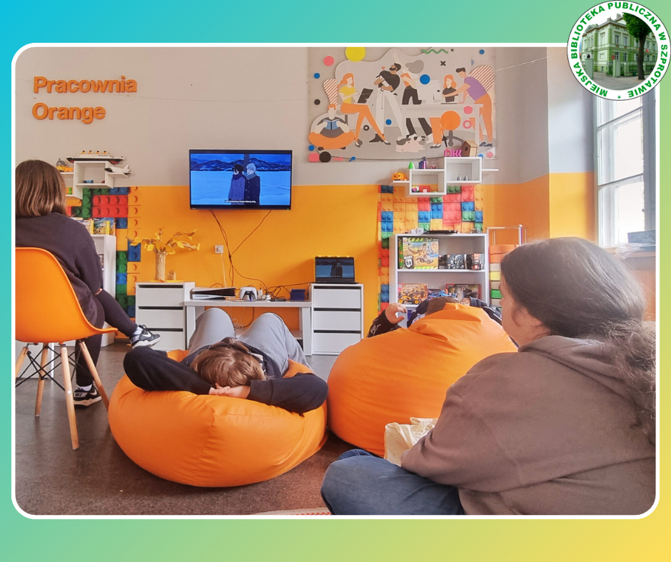 zdjęcie czworga klubowiczów w trakcie oglądania anime na telewizorze, po prawej logo biblioteki