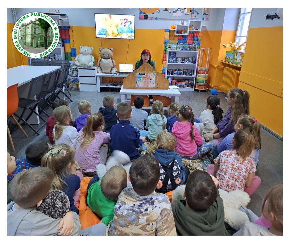 na zdjęciu prowadząca przedstawia grupie dzieci siedzących na dywanie teatrzyk kamishibai