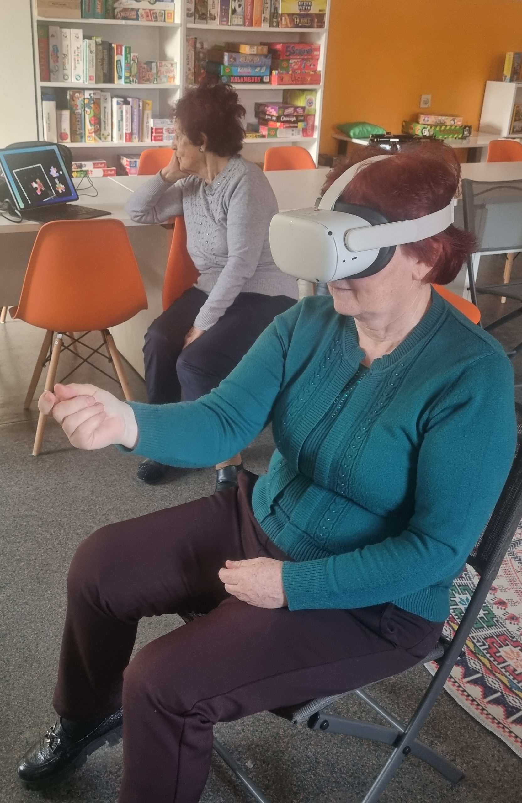 zdjęcie seniorki układającej wirtualne puzle i seniorki oglądającej grę koleżanki na podglądzie na laptopie