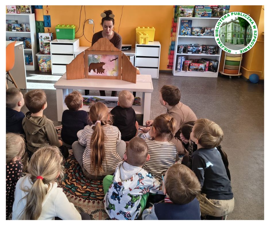 na zdjęciu prowadząca prezentuje dzieciom siedzącym na dywanie bajkę w teatrzyku kamishibai.
