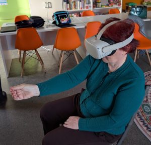 zdjęcie seniorki z wyciągniętą przed siebie ręką podczas układania wirtualnych puzli w goglach VR