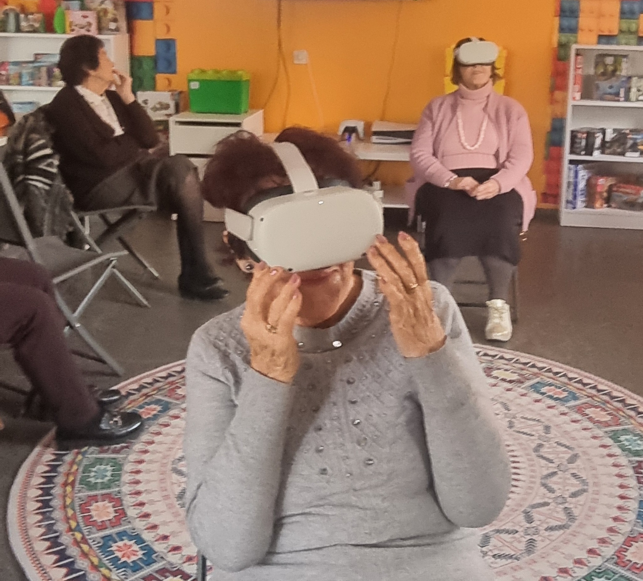 zdjęcie seniorek z goglami VR i koleżanki oglądającej ich podróże na telewizorze