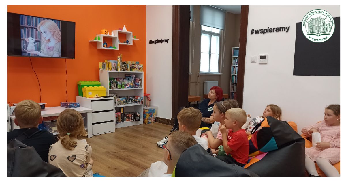 grupa dzieci z dorosłą kobietą siedzi na pufach i ogląda na ekranie bajkę, na przodzie logo mbpszprotawa