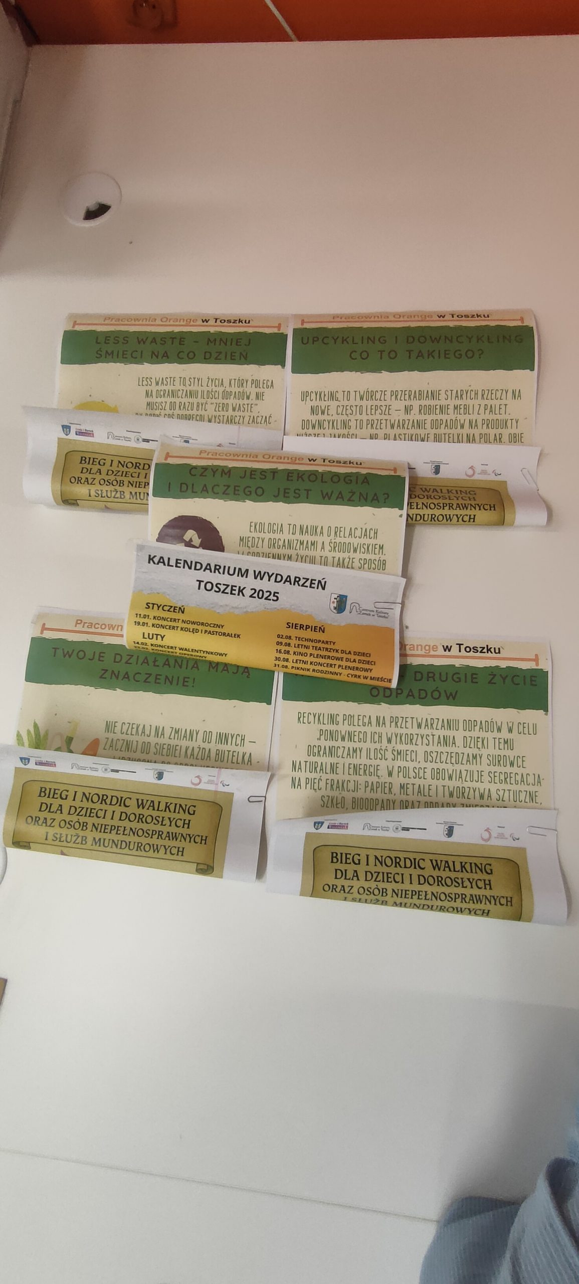 zdjęcie przedstawia plakaty leżące na stole, każdy ma zawinięty dolny brzeg.