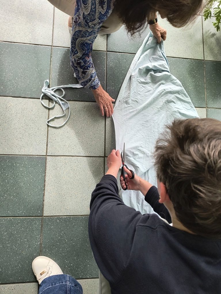 na zdjęciu dwie osoby wycinające z materiału paski na sznurki