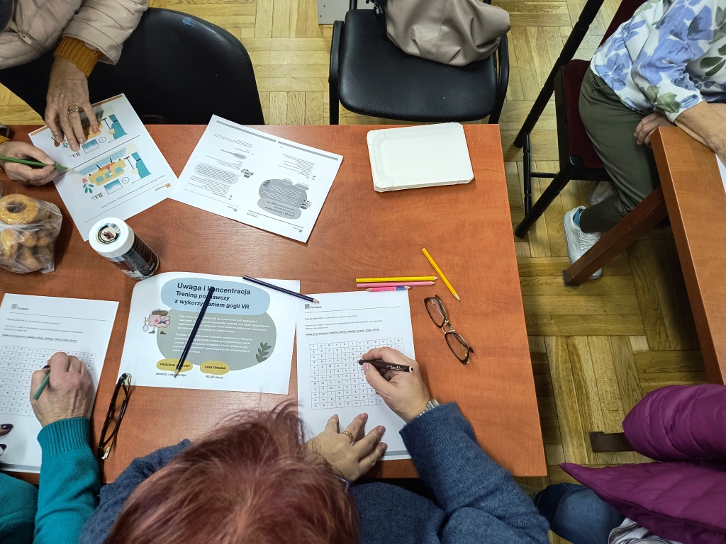 na zdjęciu widać osoby siedzące przy stołach rozwiązujących łamigłówki na kartkach