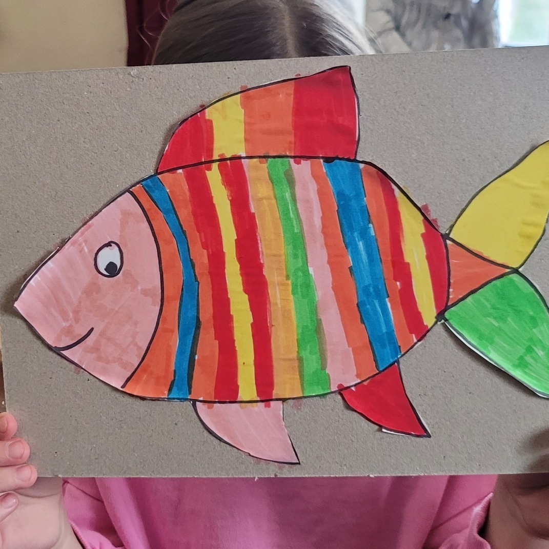 Rybka w kolorowe paski namalowana na tekturze.