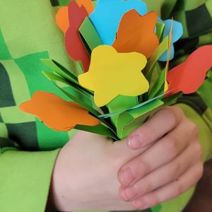 Na zdjęciu widać dłonie dziecka, a w nich wielobarwne kwiaty z papieru.