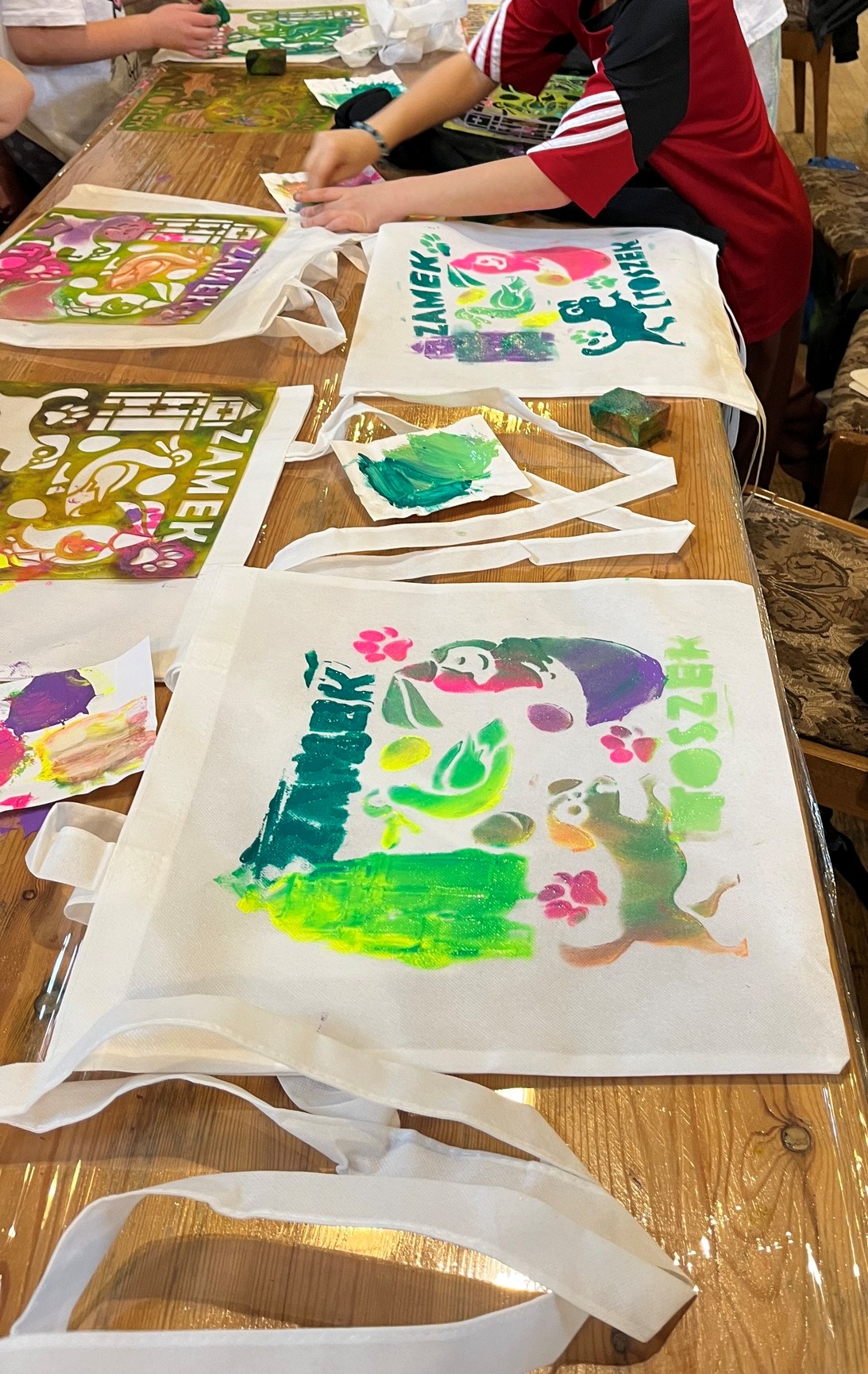 Dzieci przy stole malują farbami bawełnianą torbę.