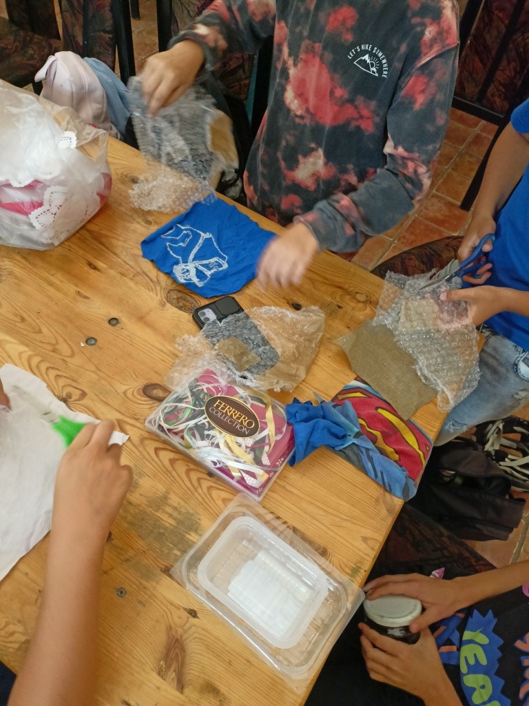 Na zdjęciu widac stół z wieloma przedmiotami, typu materiały, pudełka, wstążki itp.