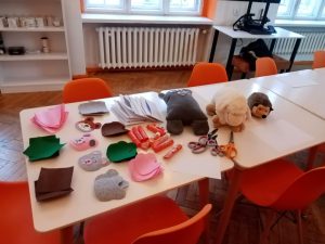 Na stole leżą materiały na spotkanie: pluszowe misie, kleje, nożyczki, koperty, papierowe głowy misiów.