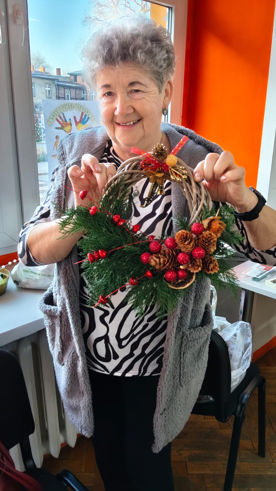 Kobieta pozuje do zdjęcia z wykonanym przez siebie stroikiem.