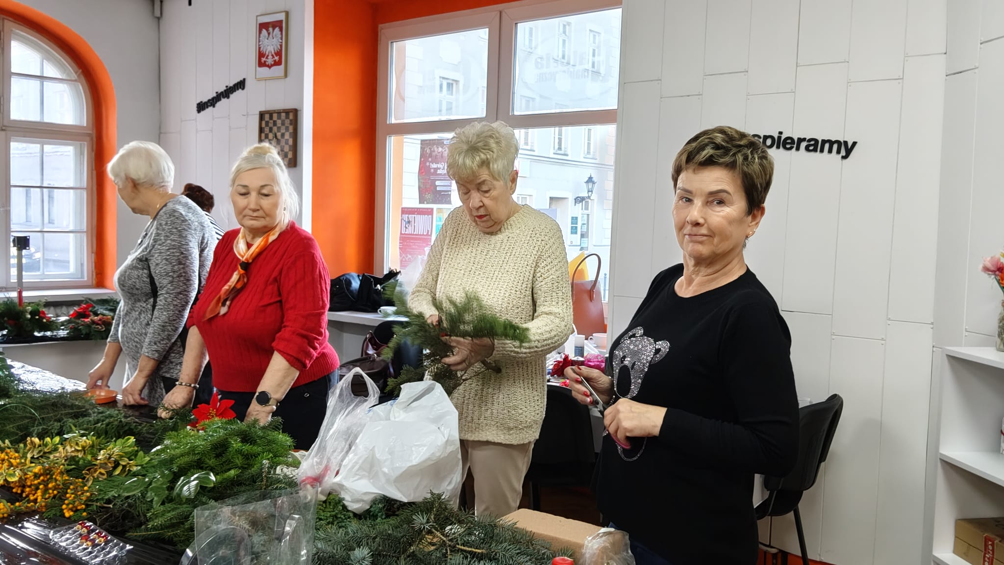 Trzy kobiety stoją przy stole na którym leży dużo gałązek igliwia.