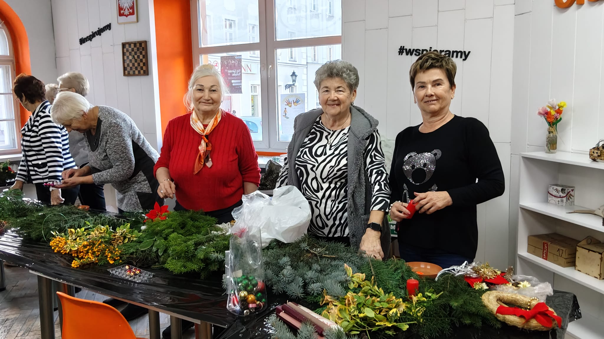 Trzy kobiety stoją przy stole na którym leży dużo gałązek igliwia.